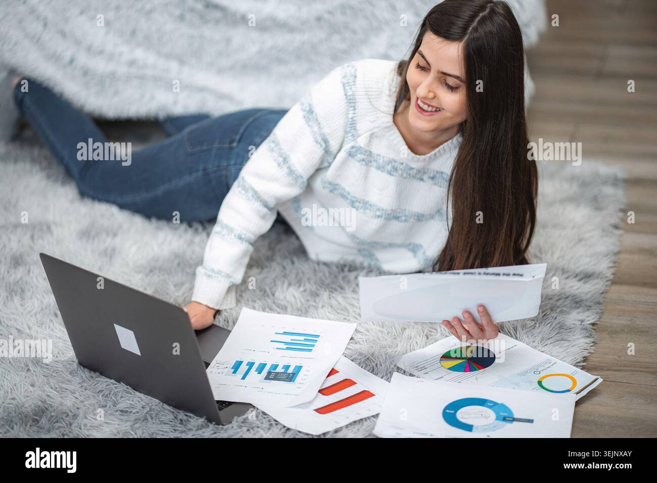 Woman lying on rug analyzing financial data using laptop Stock Photo