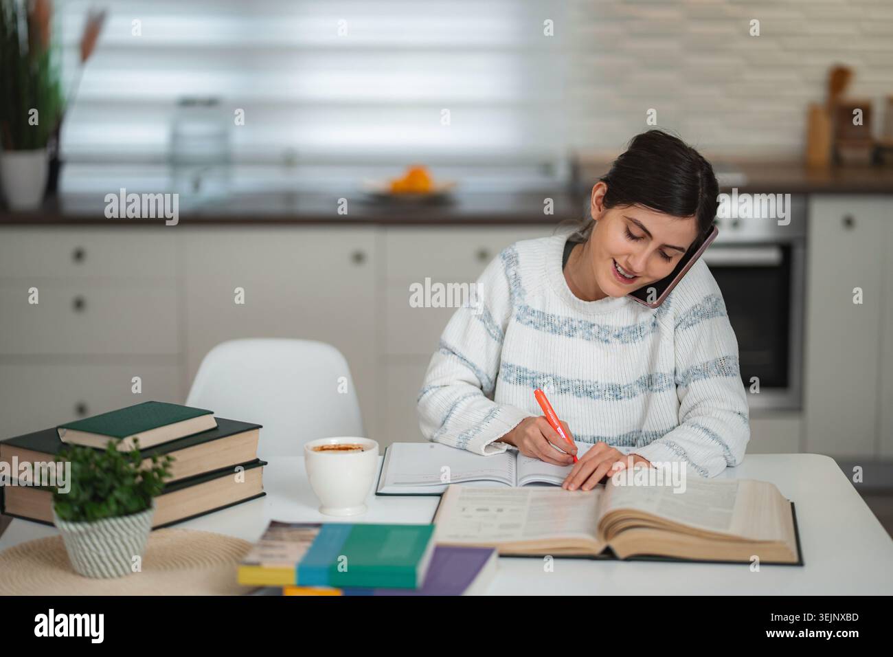 Young woman studying at home making phone call Stock Photo
