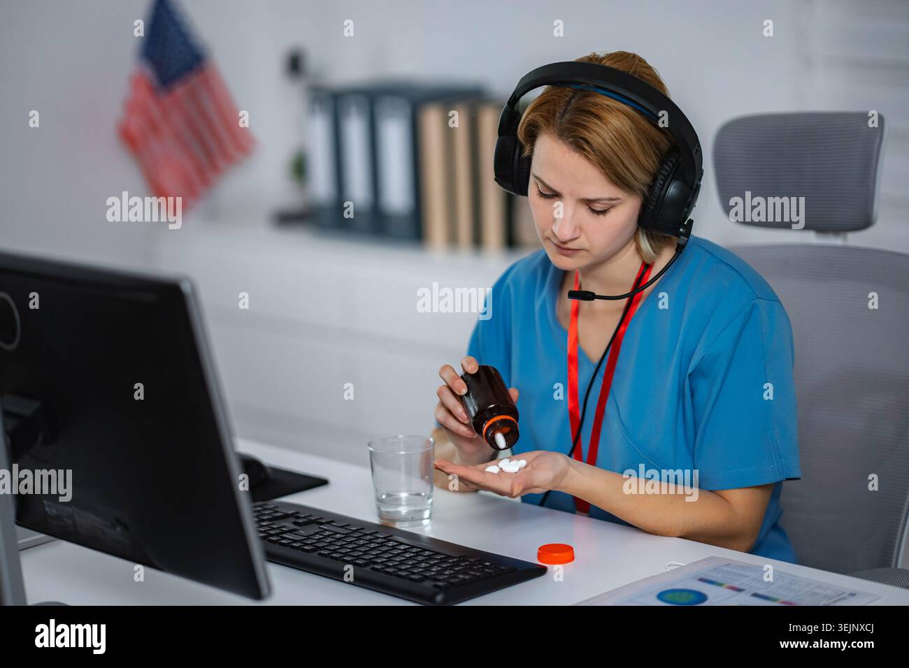 Healthcare worker taking pills at desk wearing headset Stock Photo