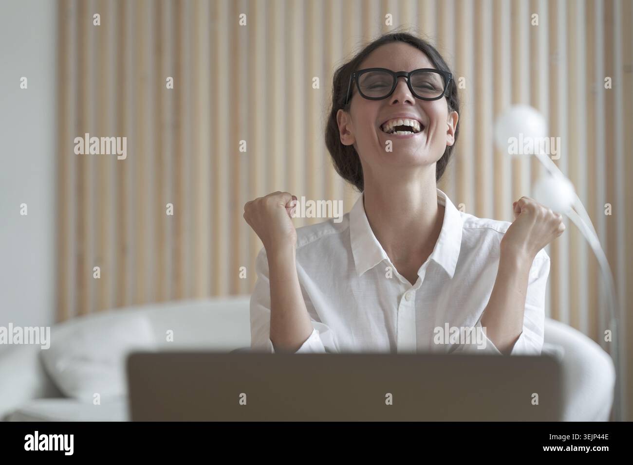 Excited italian lady clenching fists with joy while sitting in front of laptop at workplace Stock Photo