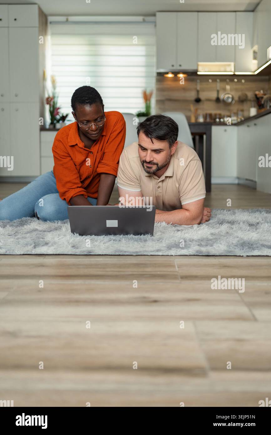 Couple lying on the floor using laptop in the kitchen Stock Photo