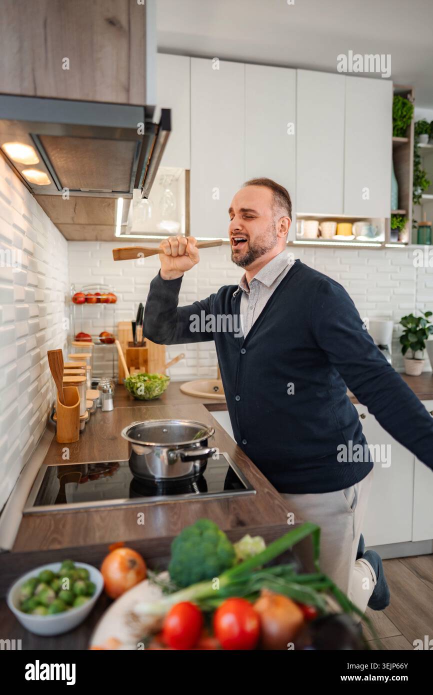Man singing in kitchen using wooden spoon as microphone Stock Photo