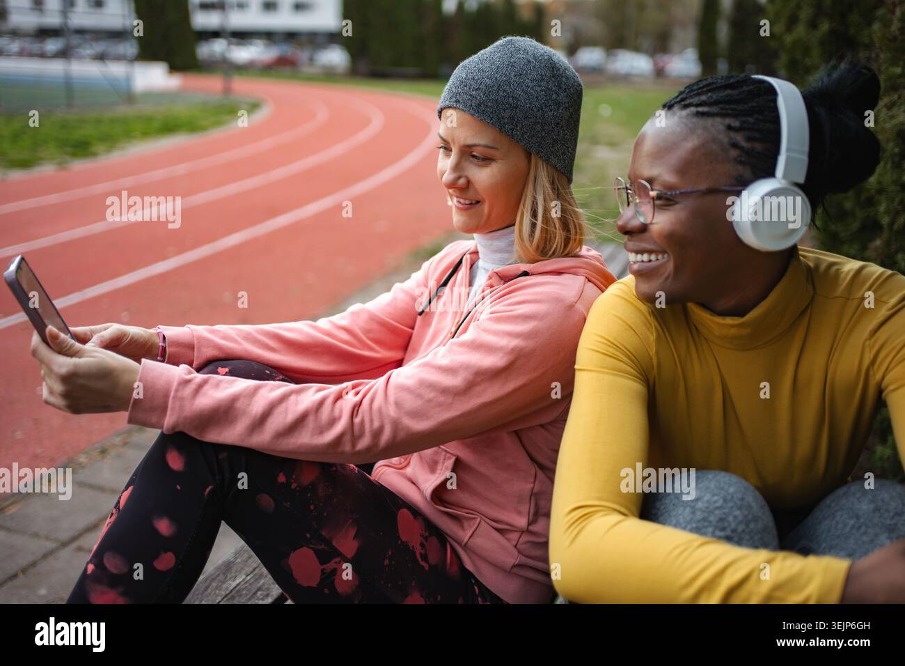 Two smiling women friends relaxing at running track using smartphone Stock Photo