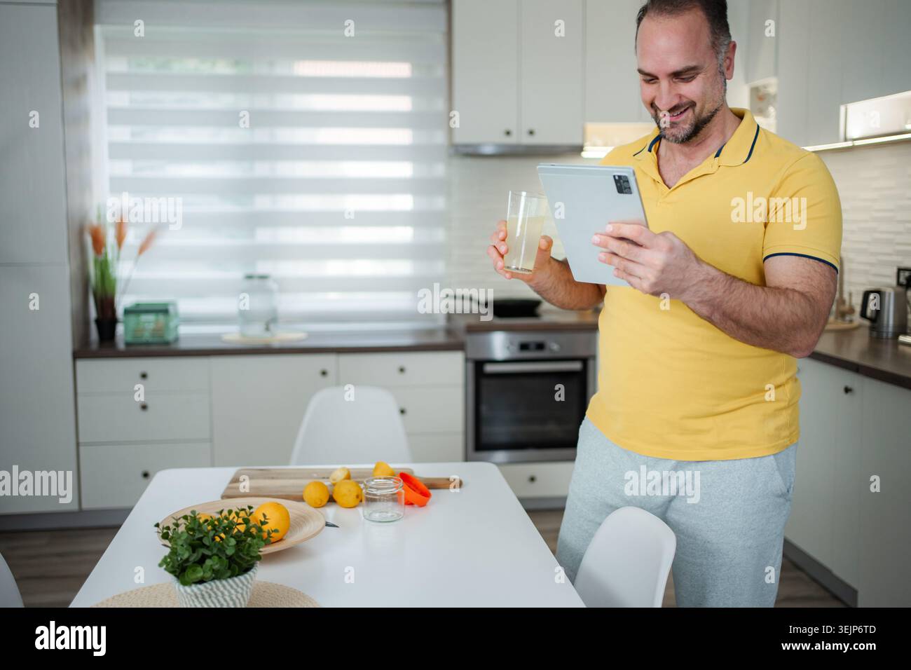 Man enjoying refreshing lemonade while using digital tablet in kitchen Stock Photo