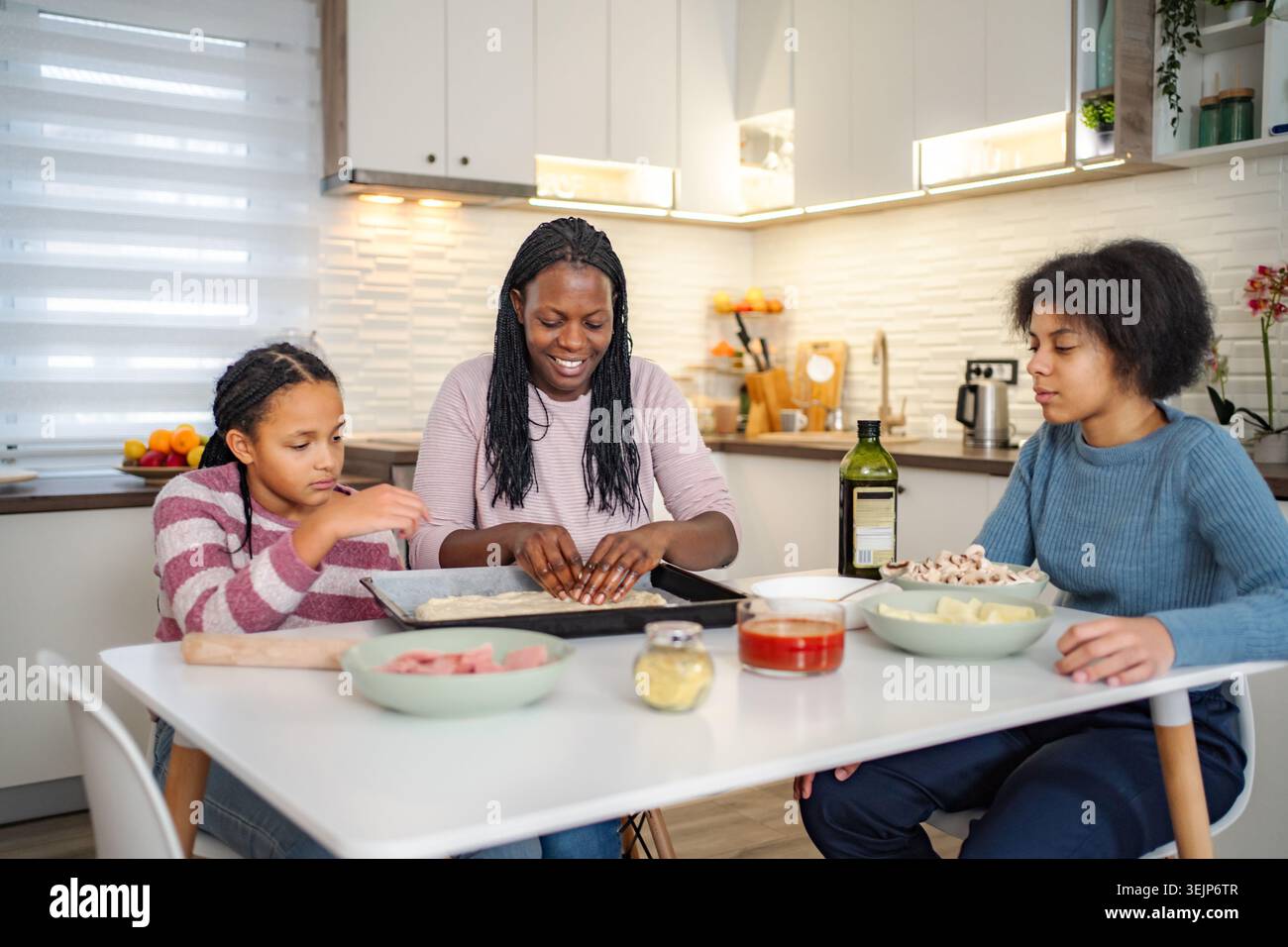 Mother and daughters preparing pizza together in kitchen Stock Photo