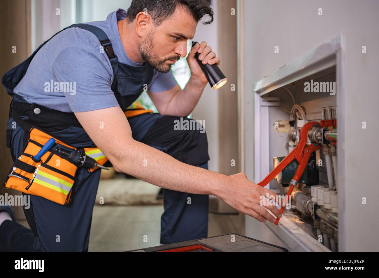 Plumber working on pipes, using flashlight and wrench Stock Photo
