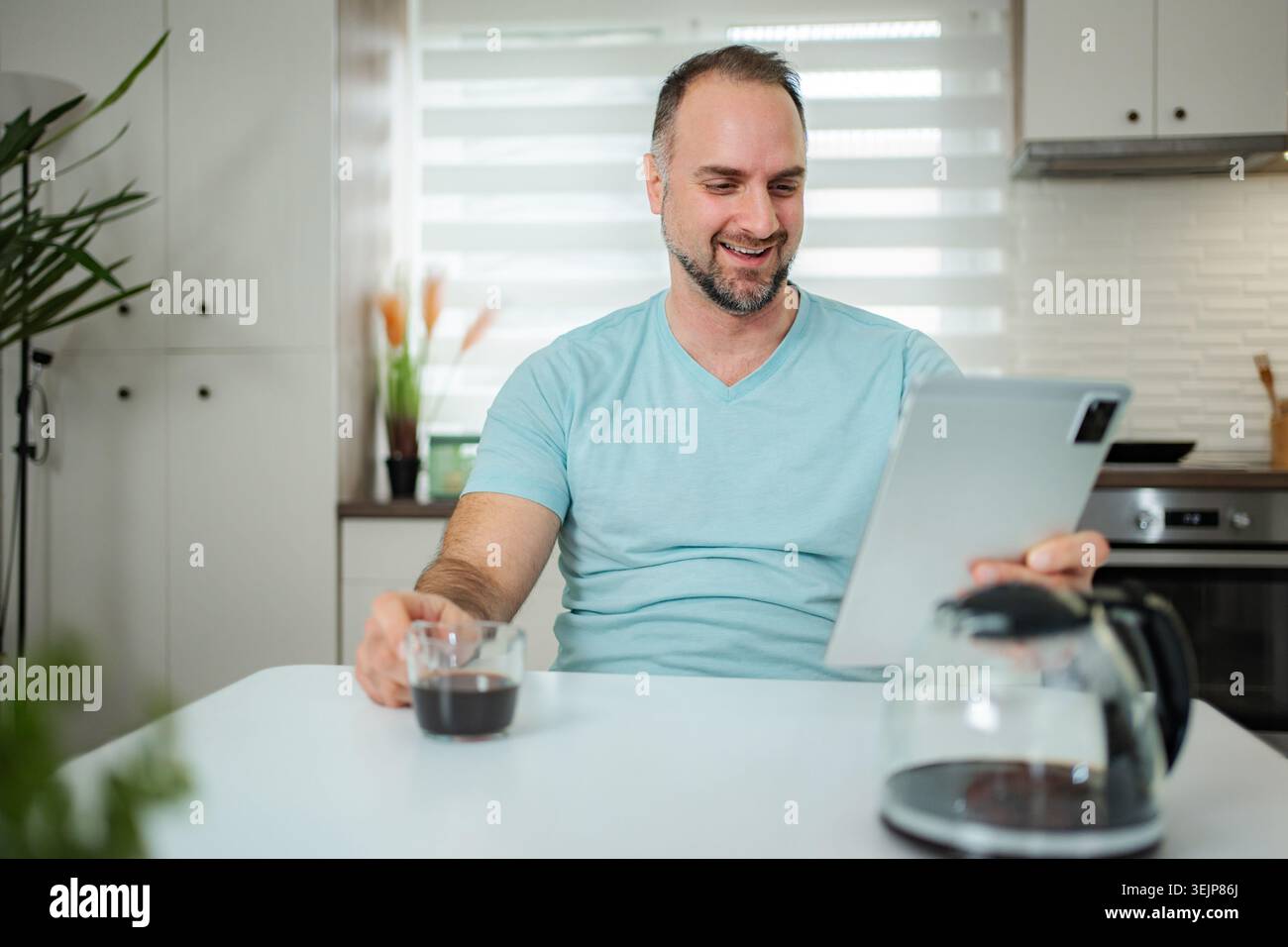 Man smiling enjoying coffee while using tablet at home Stock Photo