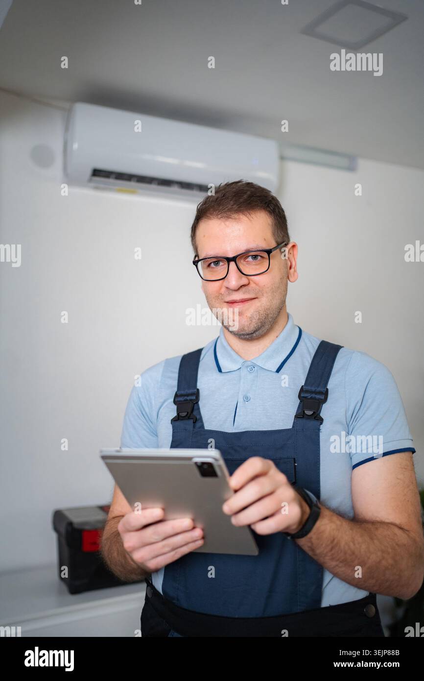 HVAC technician smiling holding digital tablet checking air conditioner Stock Photo