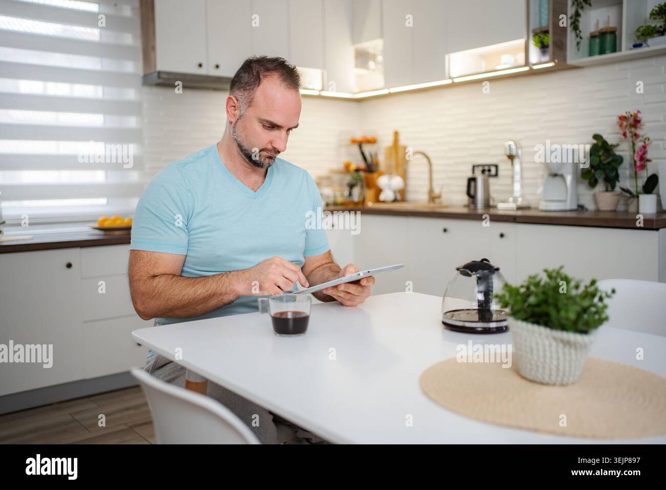 Man drinking coffee and using tablet in kitchen at home Stock Photo