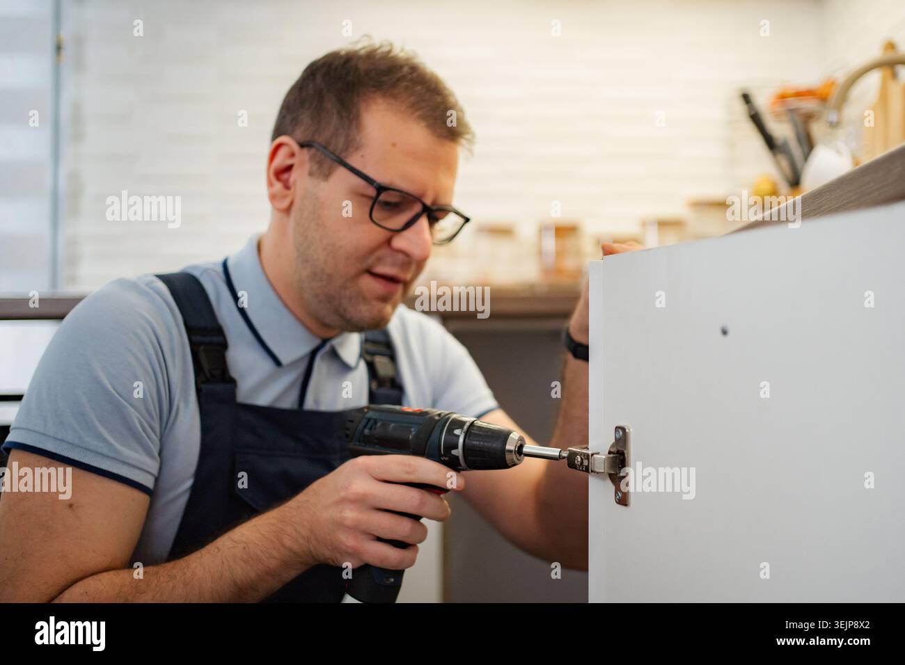 Handyman installing kitchen cabinet door using electric drill Stock Photo
