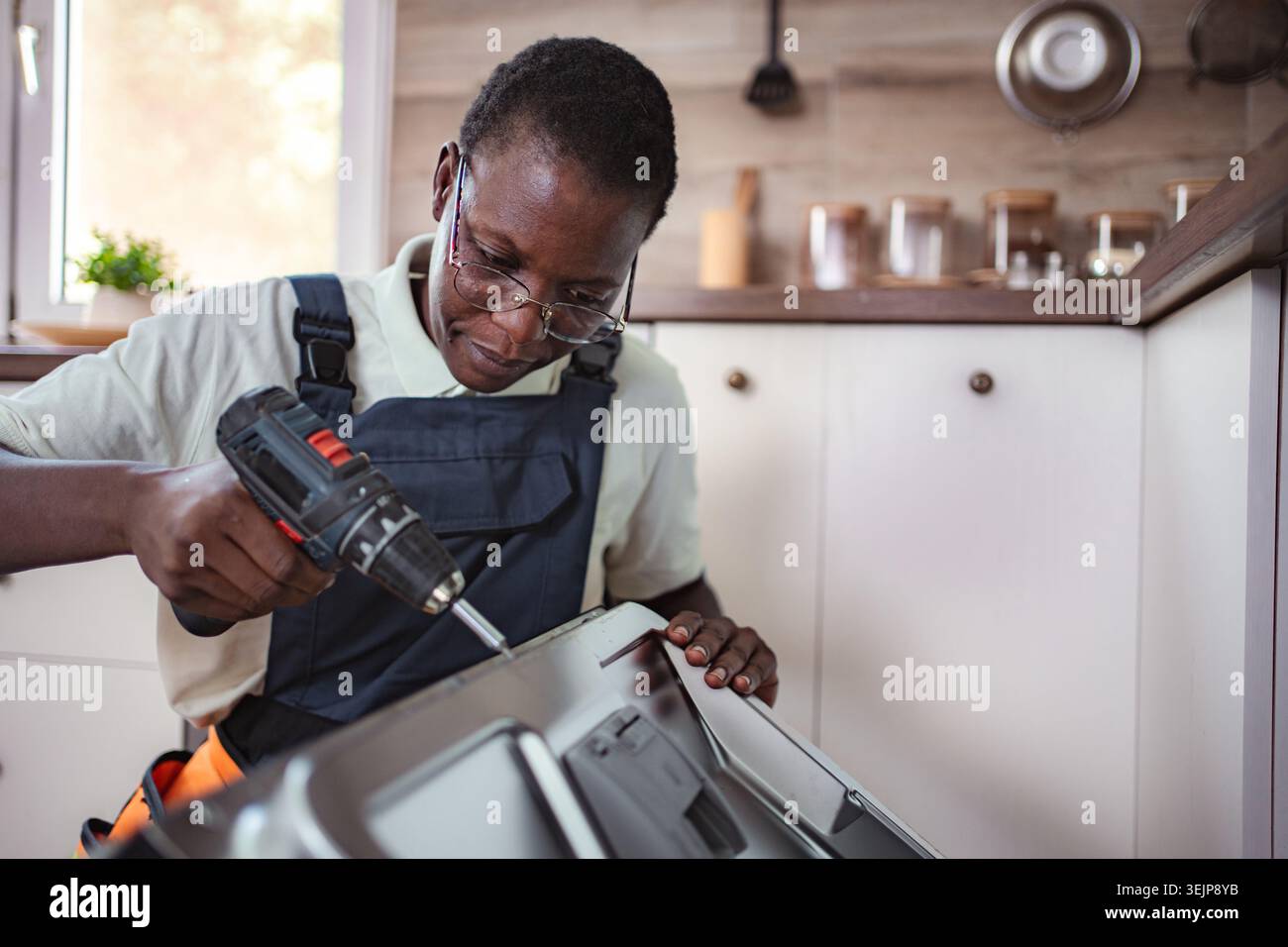 Technician repairing dishwasher using electric screwdriver in kitchen Stock Photo
