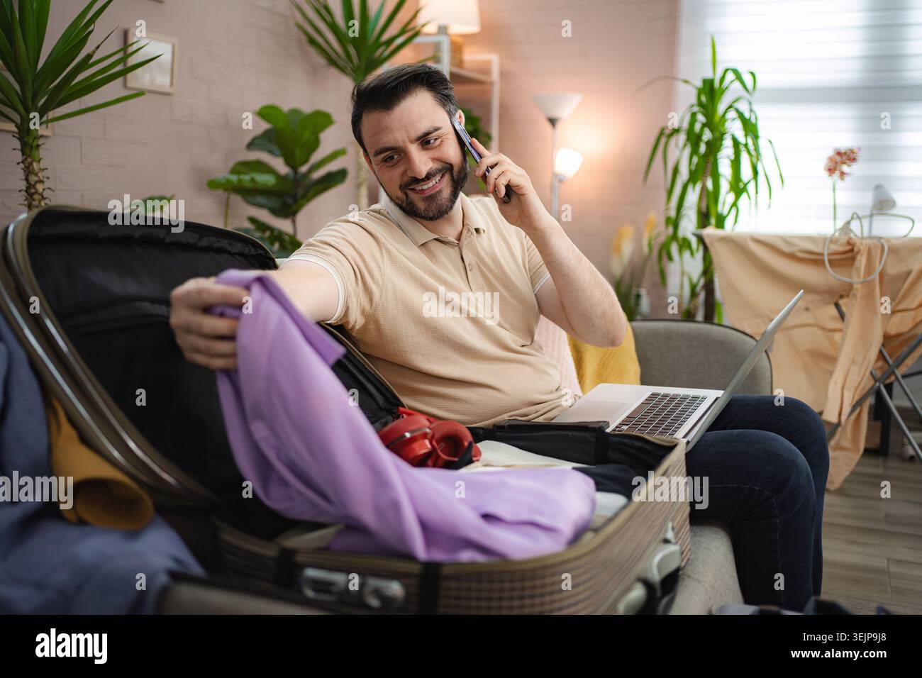 Man packing suitcase while talking on the phone Stock Photo