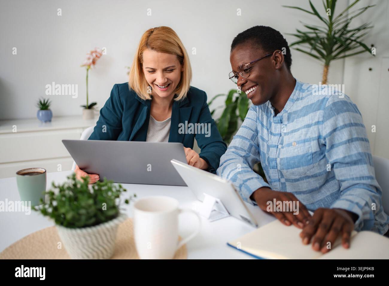 Diverse women collaborating on laptop and smiling at work Stock Photo
