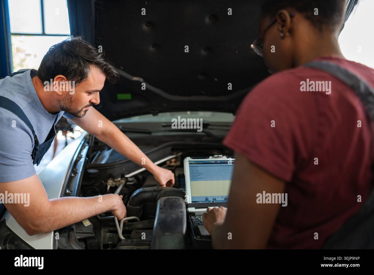 Two mechanics repairing a car engine using a computer diagnostic software Stock Photo