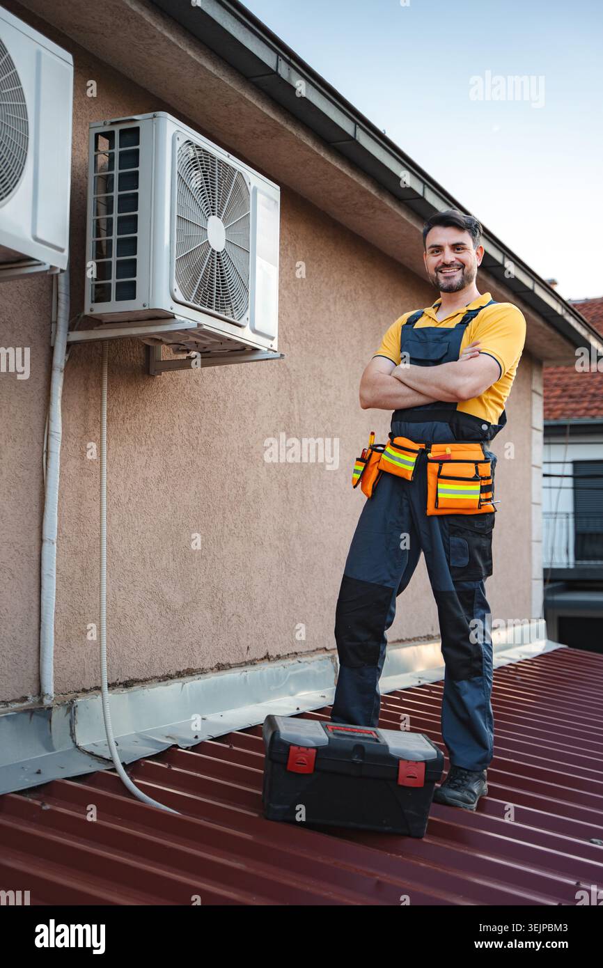 Hvac technician posing with arms crossed after installing an air conditioner on a rooftop Stock Photo