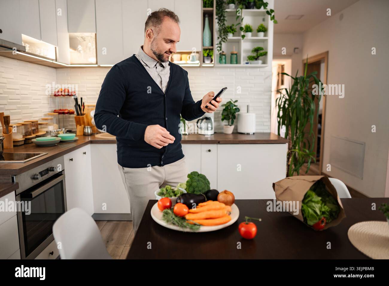 Man using smartphone checking ingredients in kitchen Stock Photo