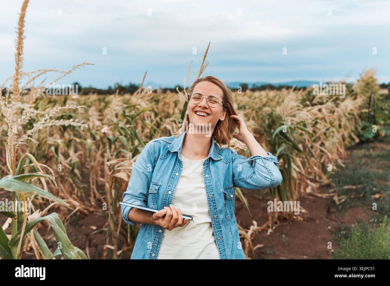 Farmer smiling and holding tablet in corn field Stock Photo
