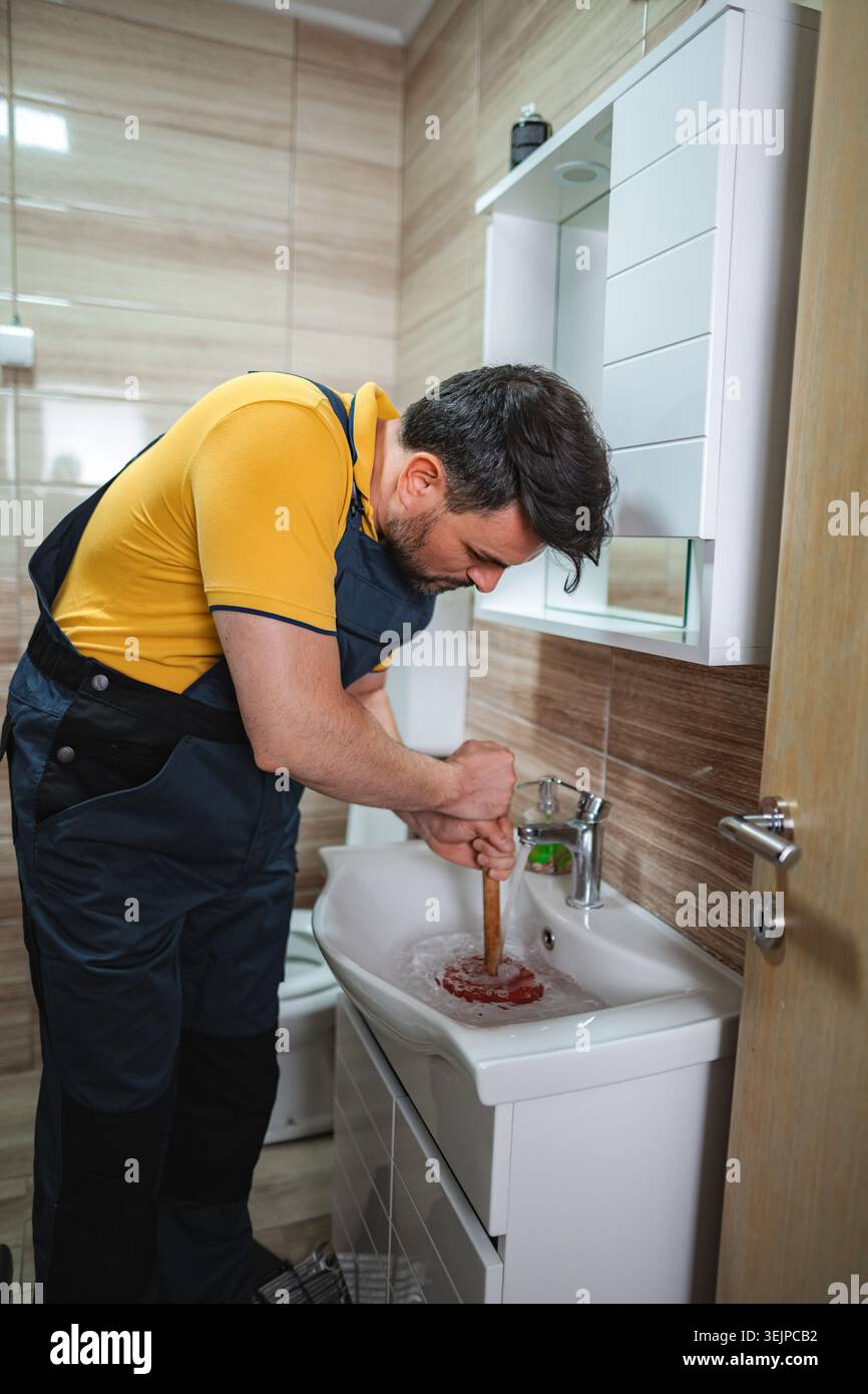 Plumber using plunger in bathroom sink Stock Photo
