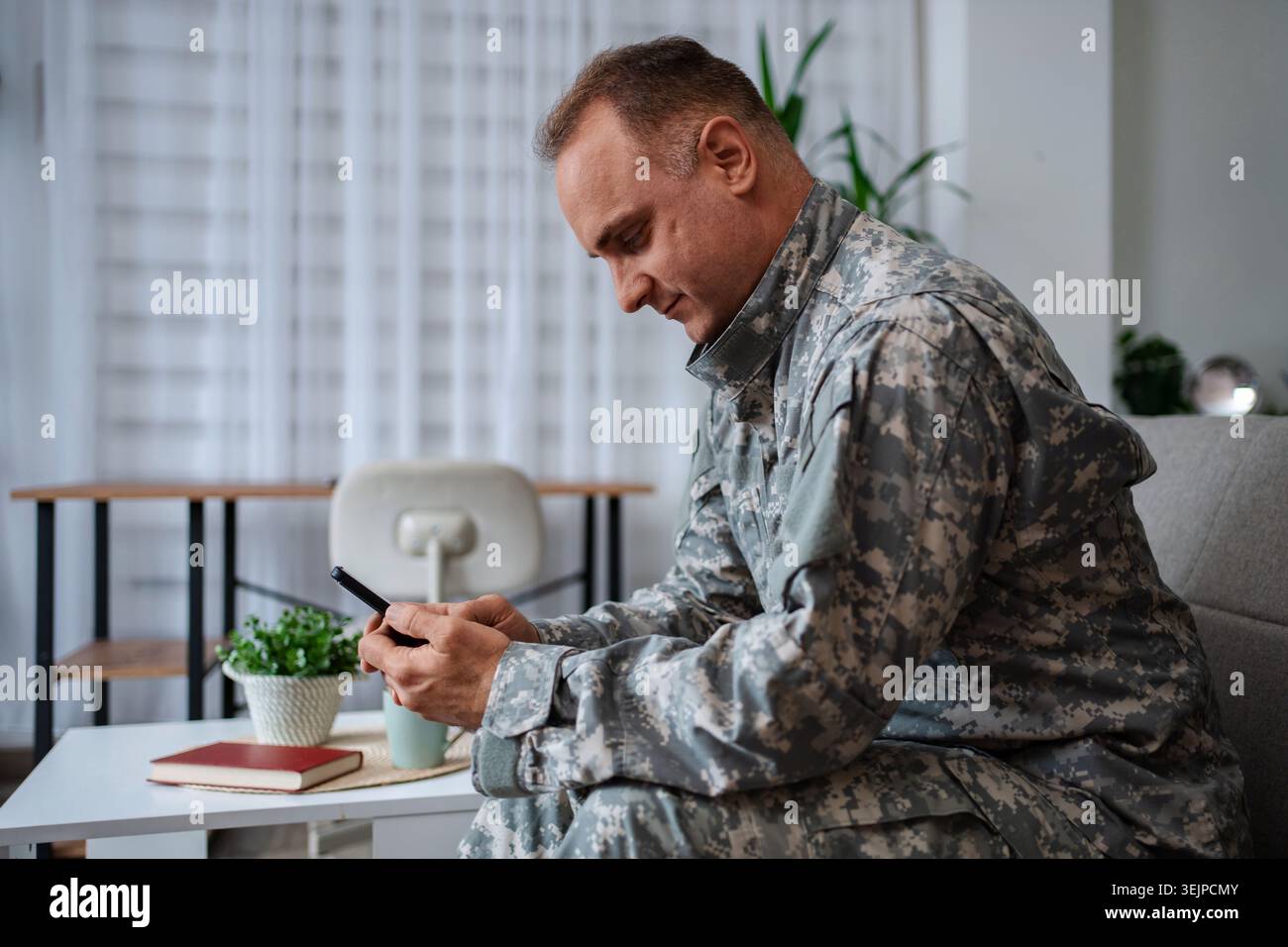 Soldier in camouflage uniform using smartphone at home Stock Photo