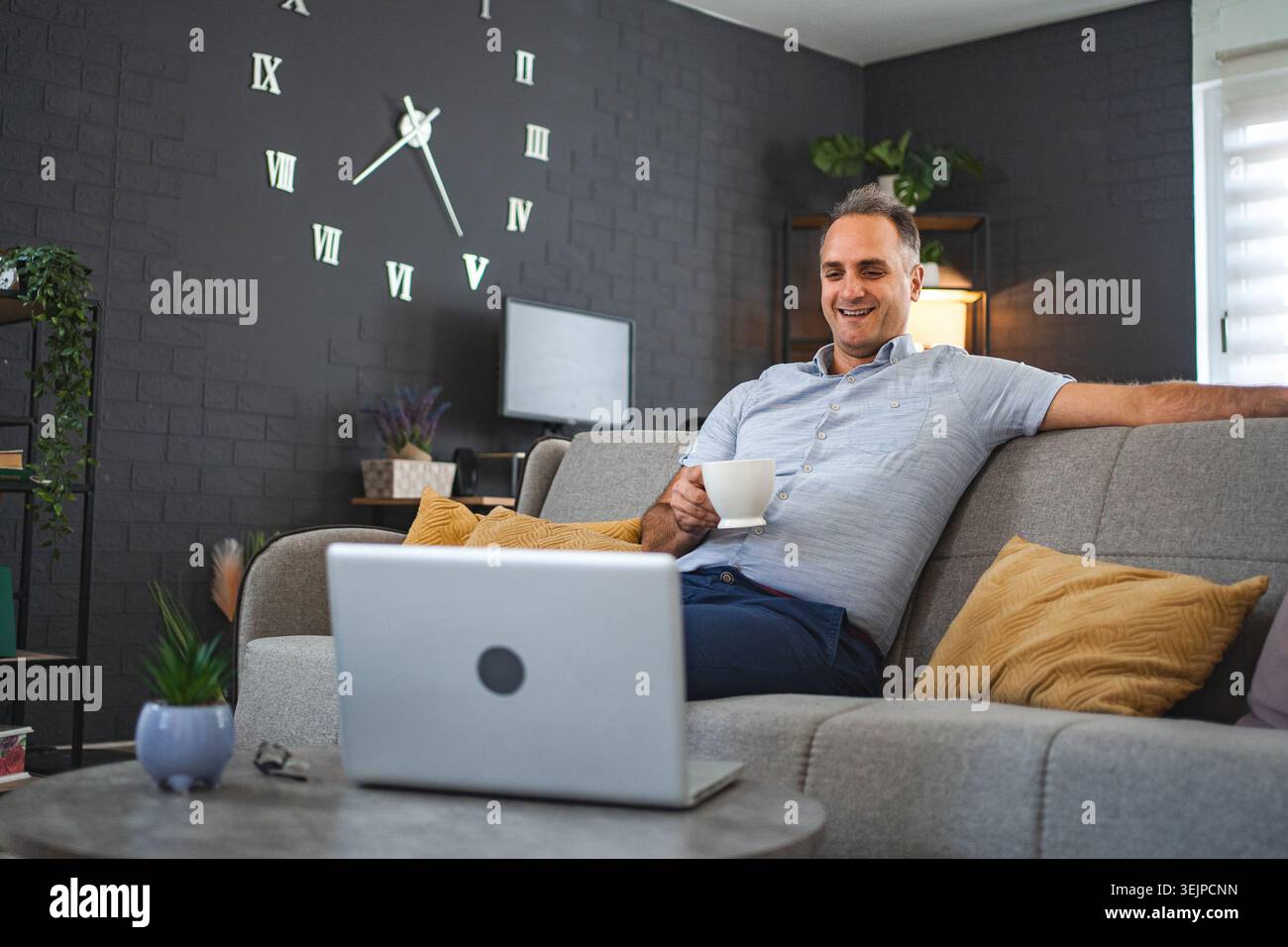 Middle aged Caucasian man sitting on the sofa watching videos on laptop Stock Photo