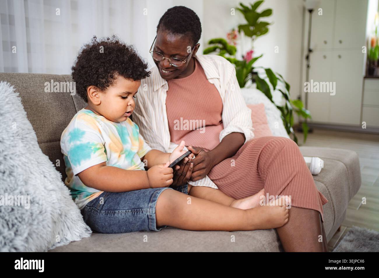 Mother and son using smartphone together on couch Stock Photo