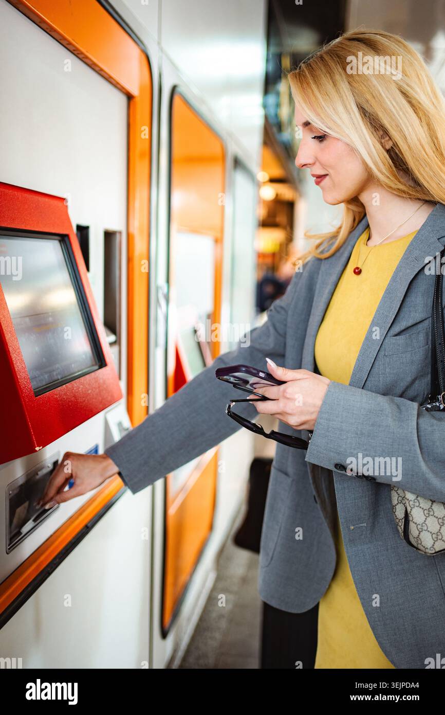 Young adult woman using a ticket vending machine at a public transport ...