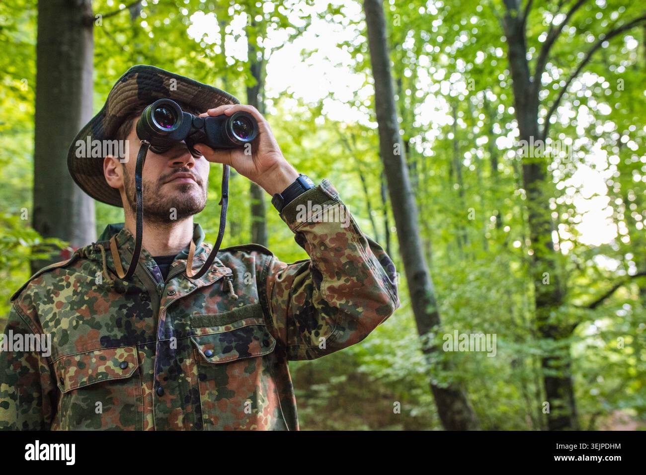 Soldier wearing camouflage uniform using binoculars in forest Stock Photo