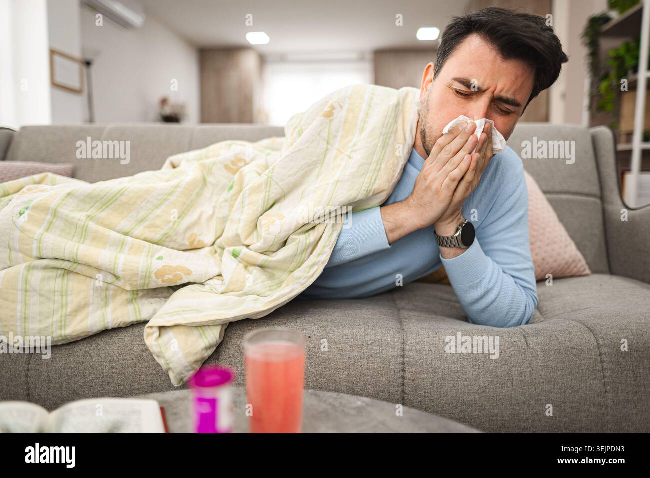 Sick man having a runny nose while lying on a sofa covered with blanket Stock Photo
