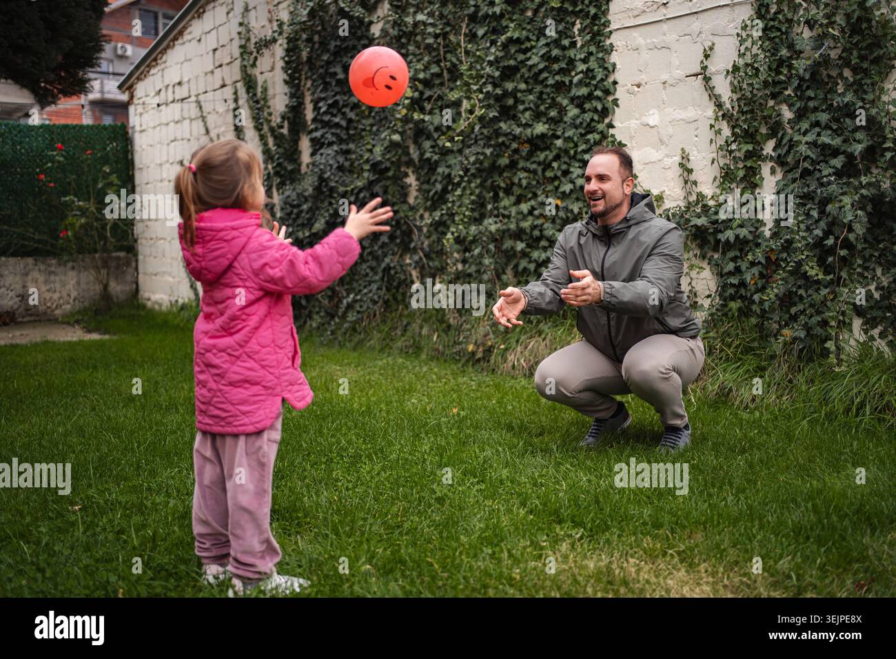 Father and daughter playing catch with orange ball in backyard Stock Photo