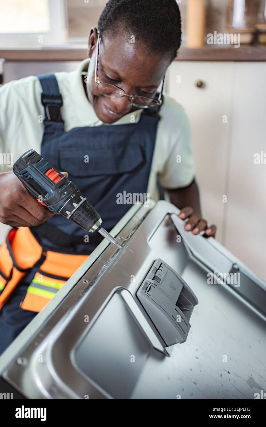 Technician repairing dishwasher using electric screwdriver in a kitchen Stock Photo