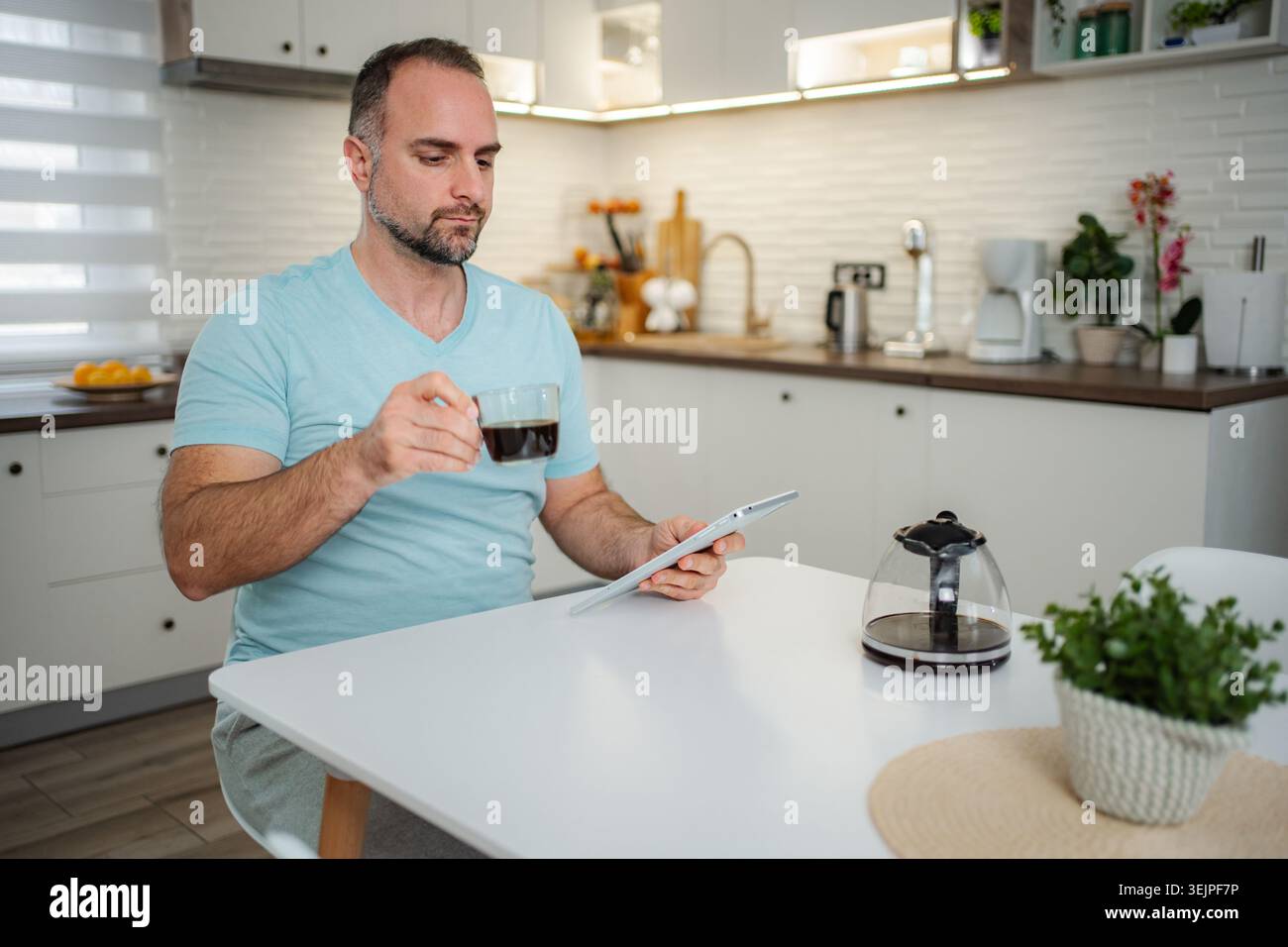 Adult man drinking coffee and using tablet in kitchen Stock Photo