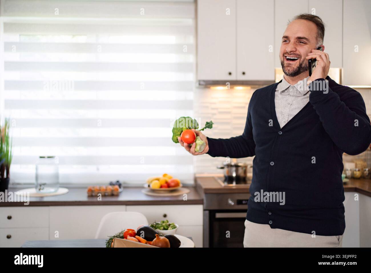 Man talking on phone holding vegetables in kitchen Stock Photo