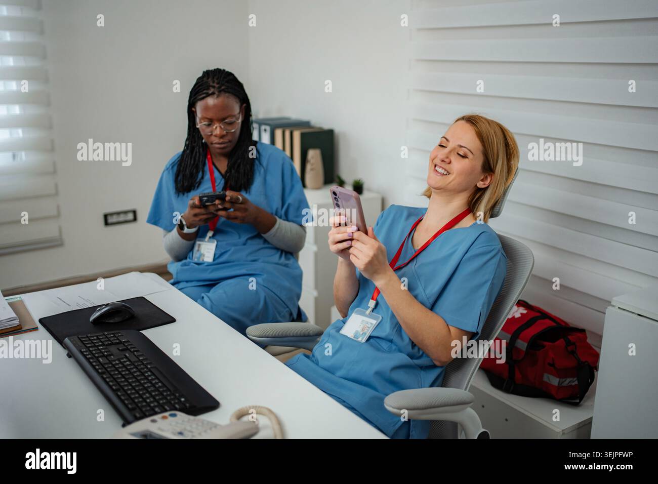 Nurses relaxing using cell phones during break laughing Stock Photo