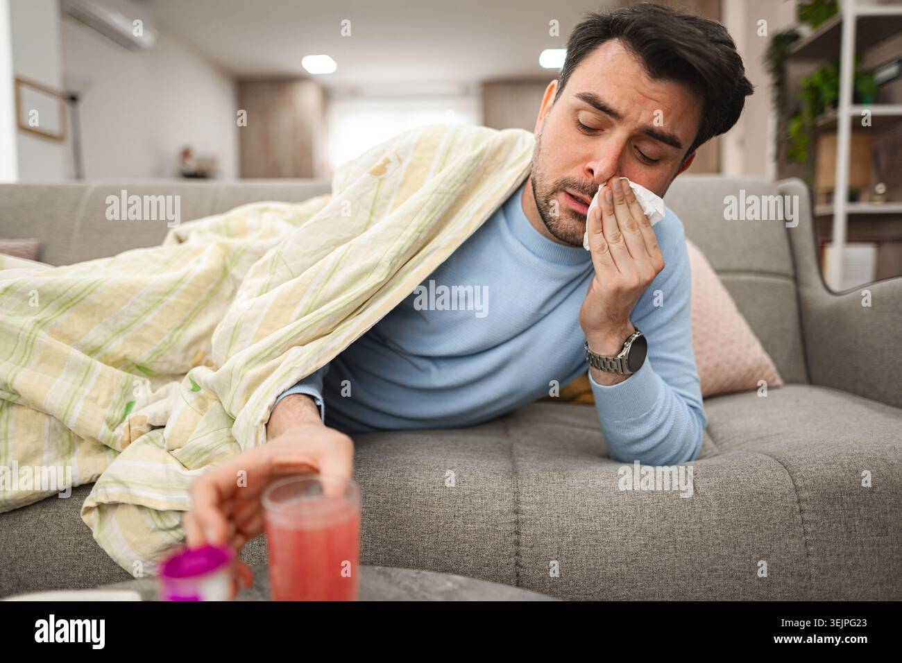 Sick man having a runny nose while lying on a sofa covered with blanket Stock Photo