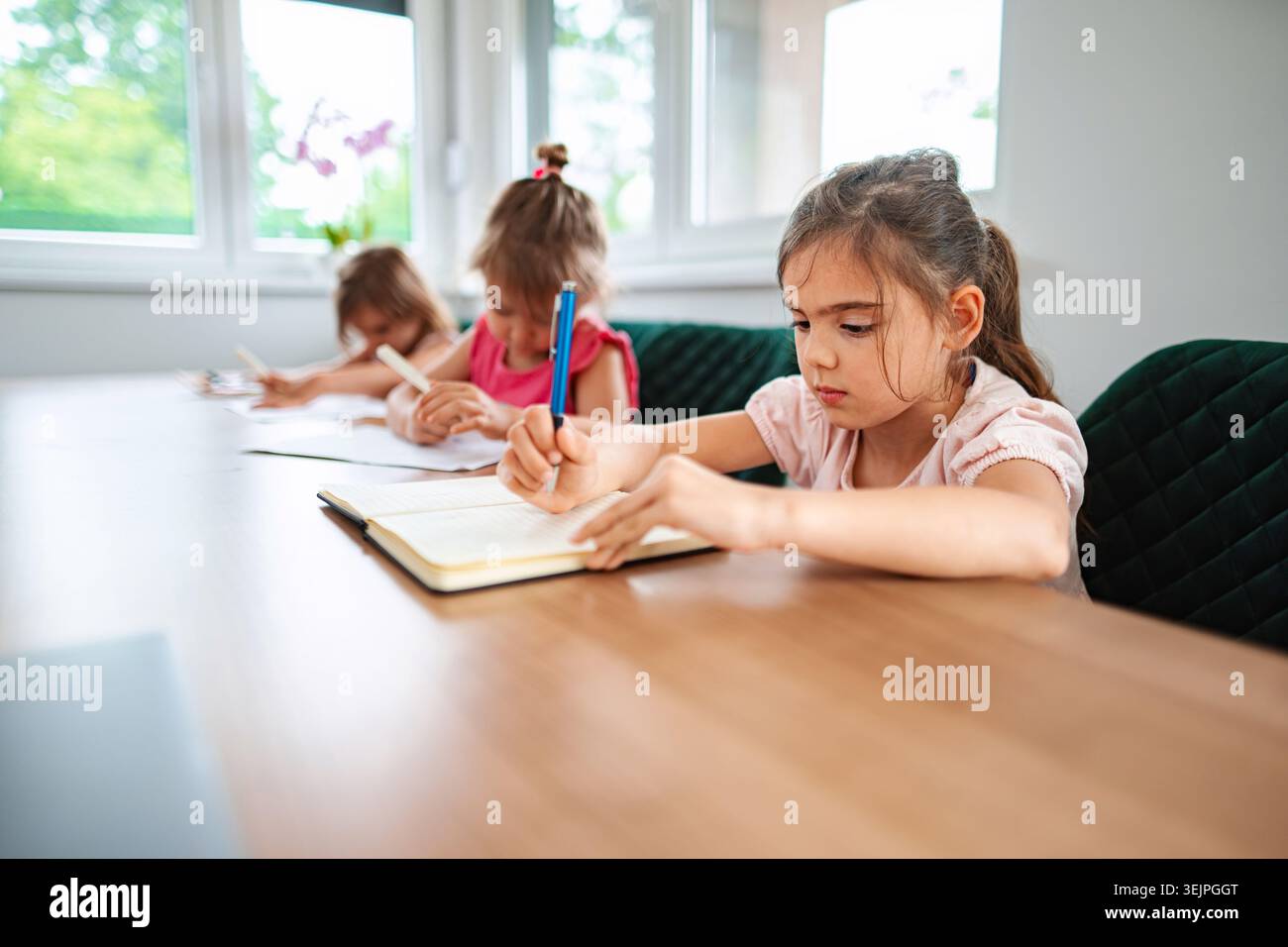 Children engaged in creative writing at a sunlit table Stock Photo