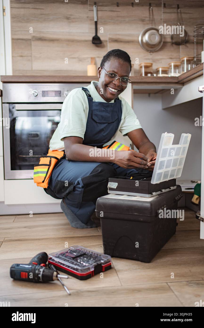 Smiling african american female plumber fixing pipes under kitchen sink Stock Photo