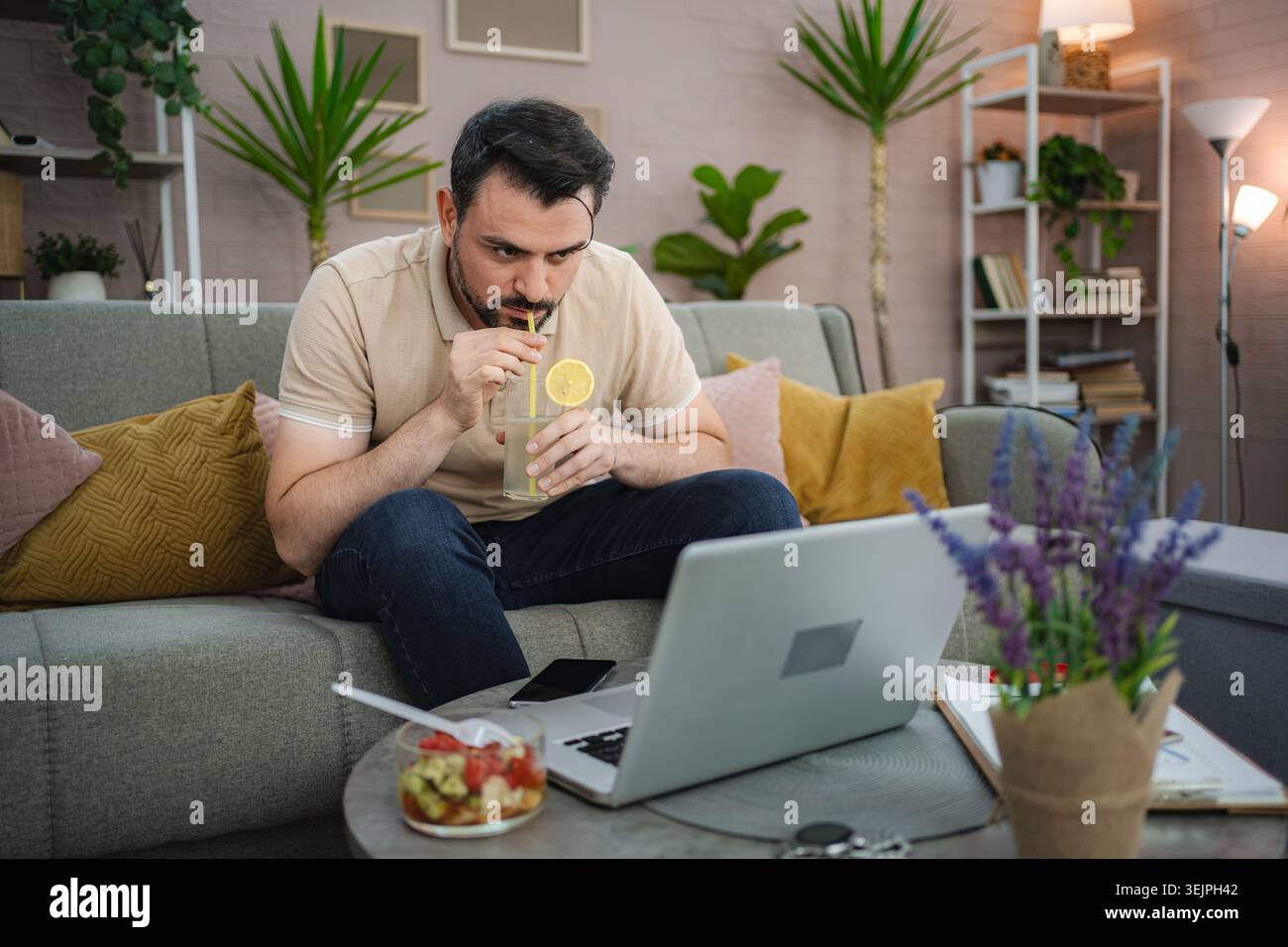 Freelancer drinking lemonade and working from home on laptop Stock Photo