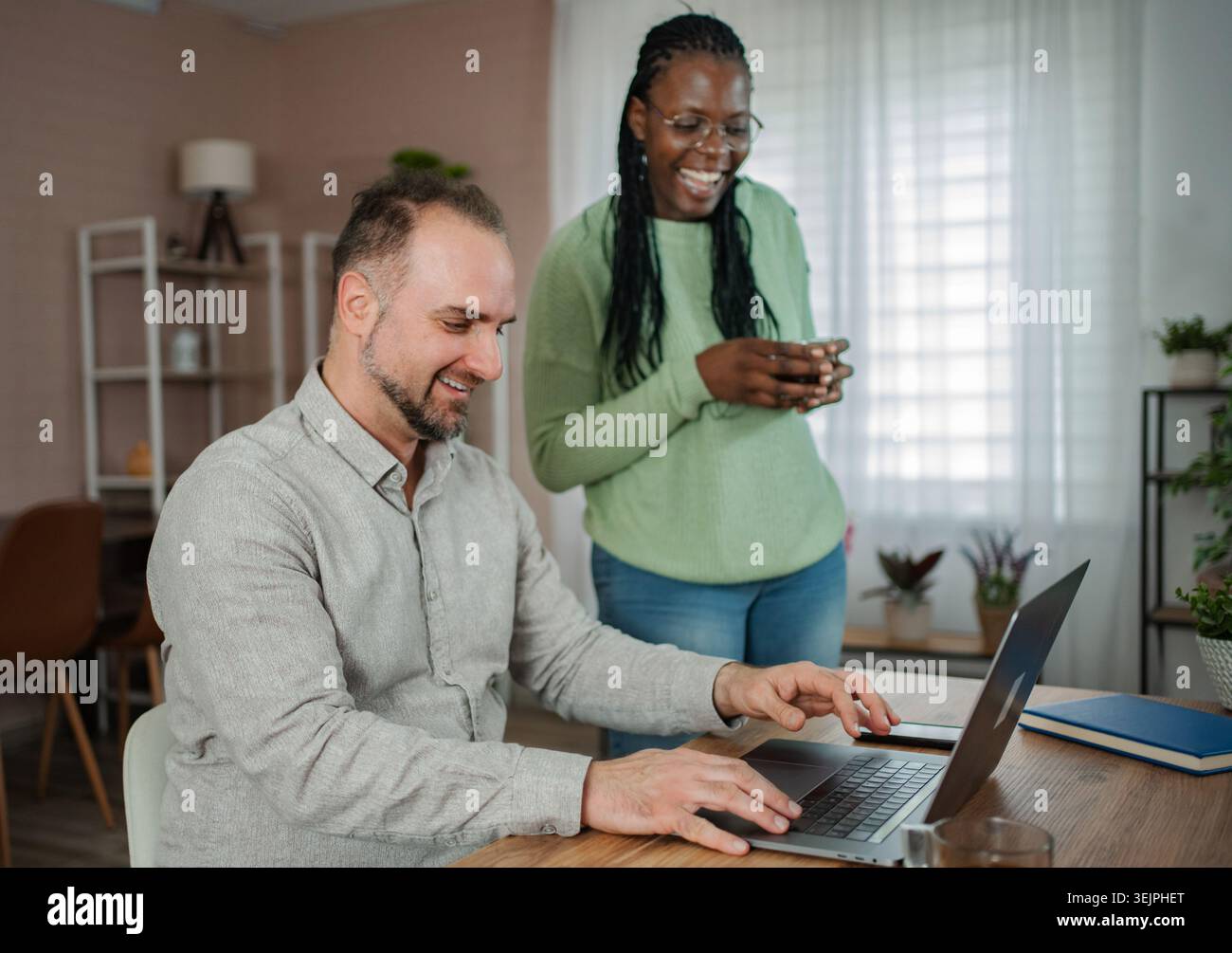 Happy multicultural couple collaborating and laughing while working remotely at home Stock Photo