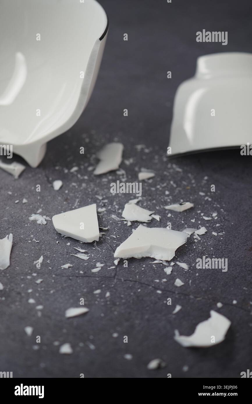 Broken white ceramic bowl lies on a dark surface Stock Photo