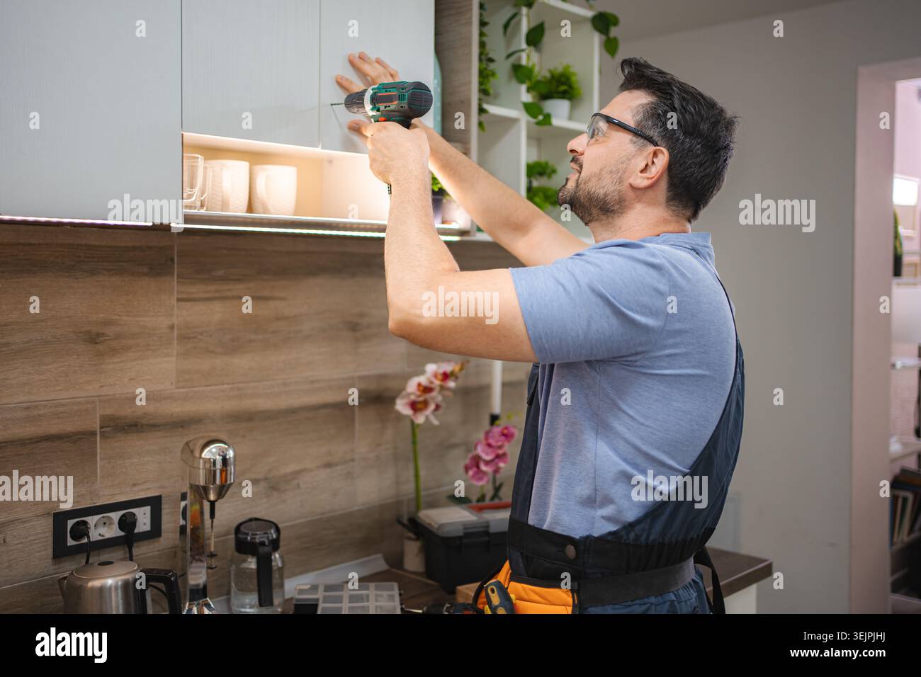 Handyman installing kitchen cabinets using a cordless screwdriver Stock Photo