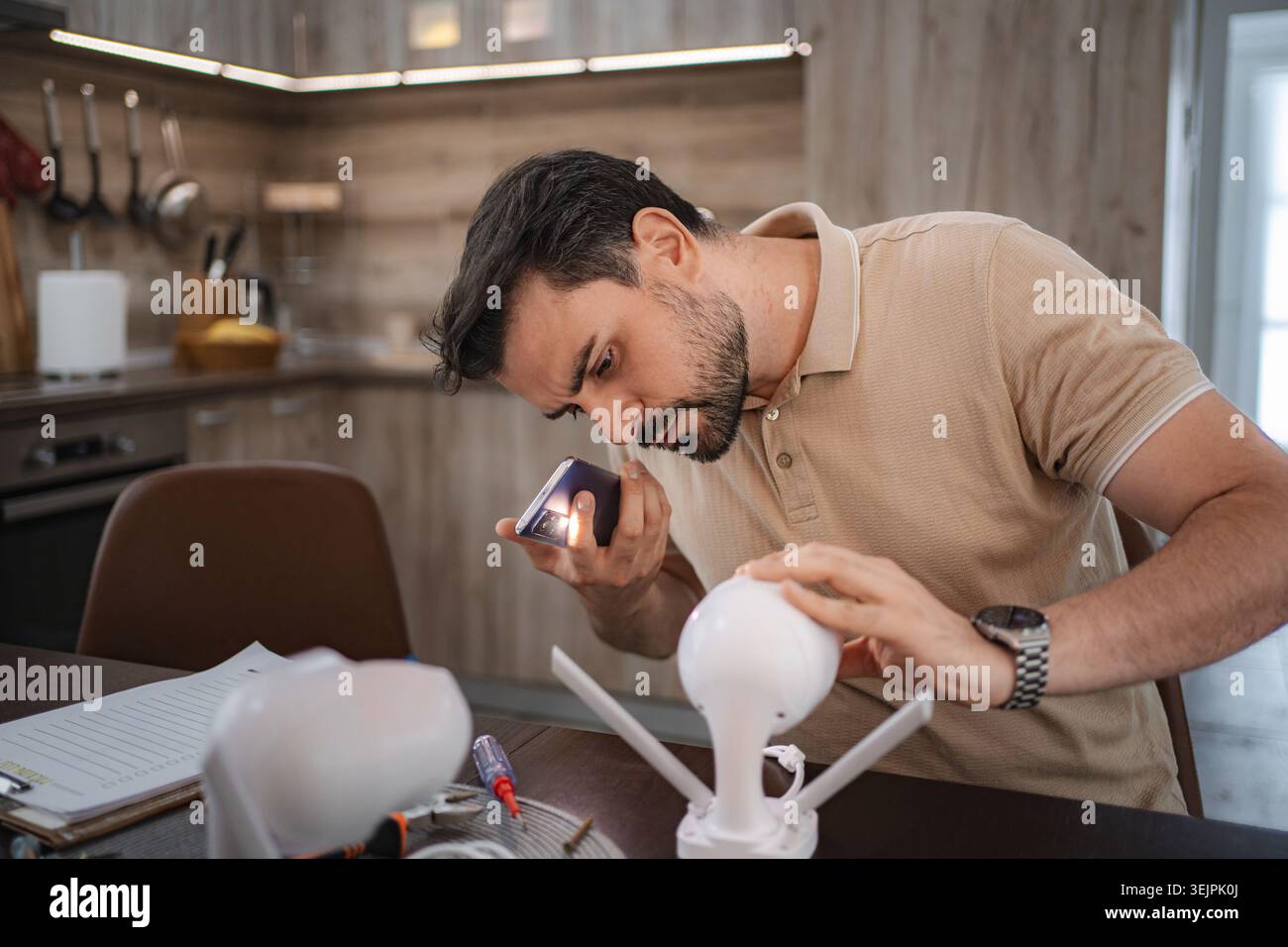 Technician repairing cctv camera using smartphone flashlight in kitchen Stock Photo