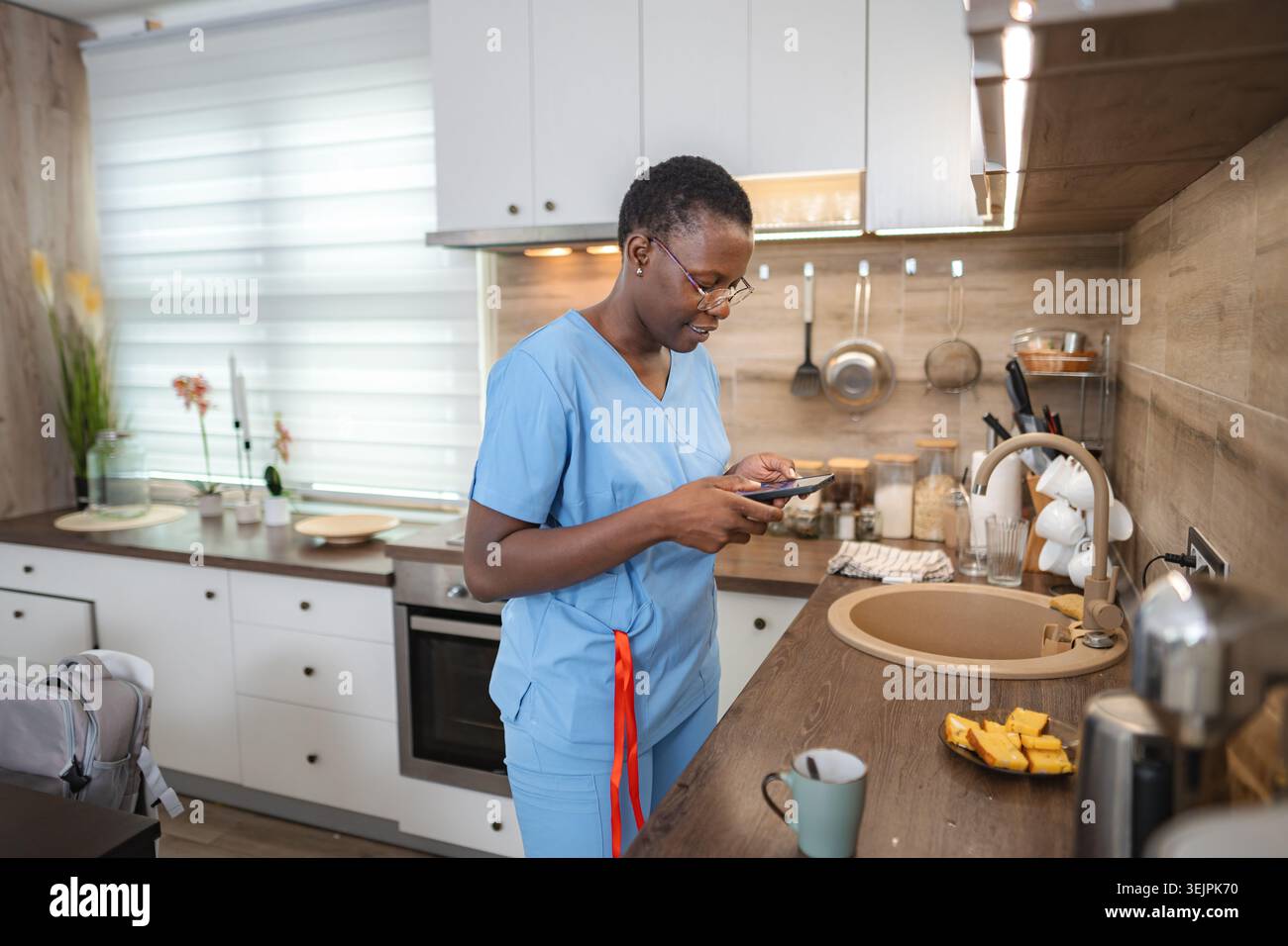 Nurse using smartphone in kitchen during break time Stock Photo