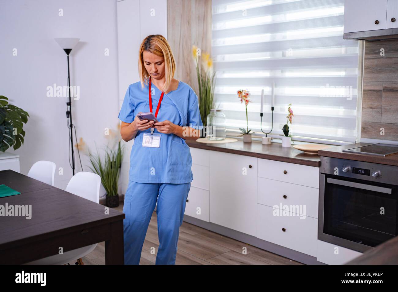 Female Doctor Using Smartphone at Home in her Kitchen Stock Photo