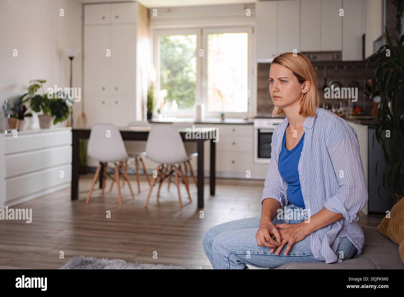 Young woman sitting on sofa feeling lonely at home Stock Photo