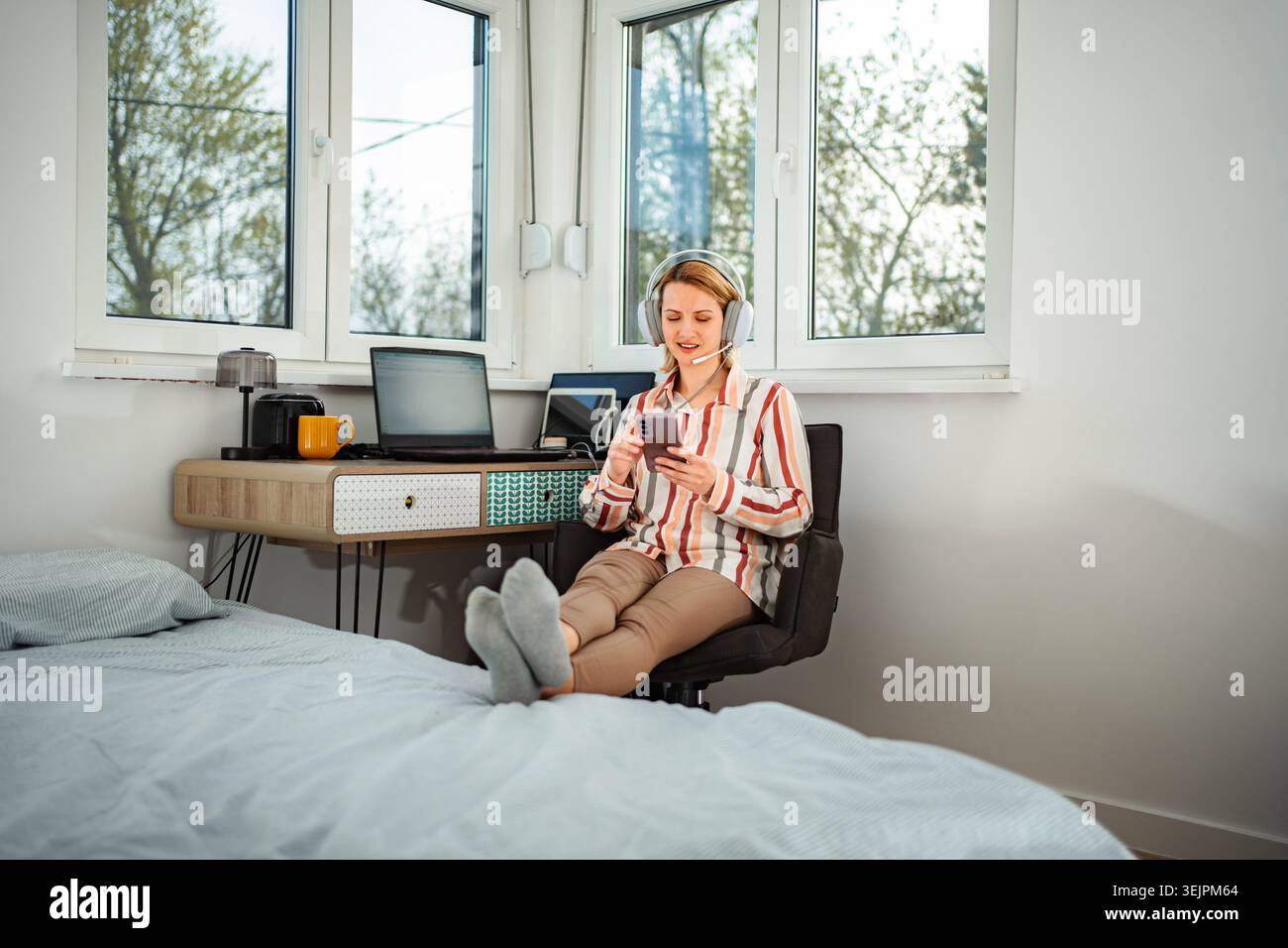 Woman working from home using headset and smartphone Stock Photo