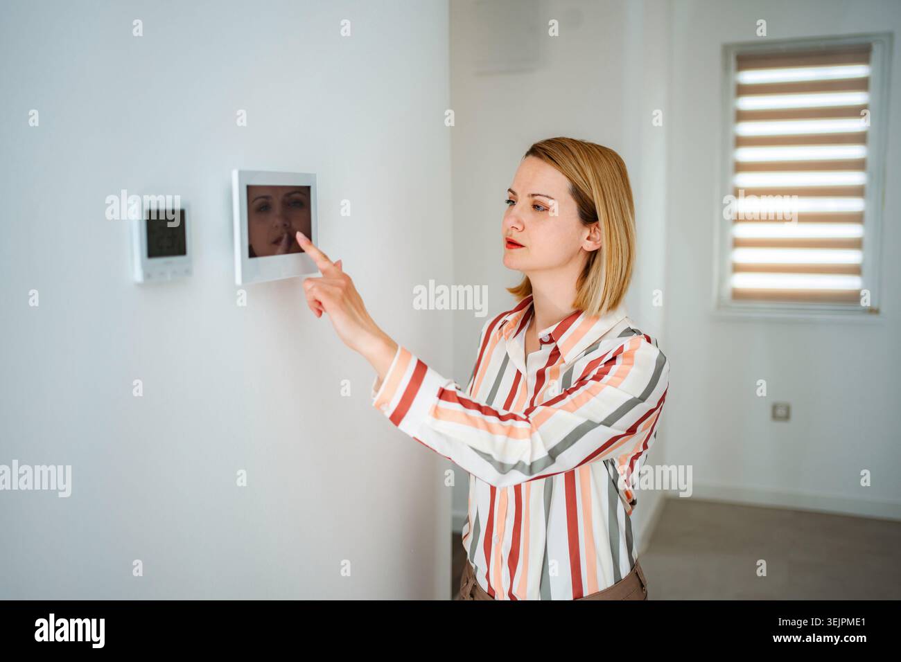 Woman interacting with smart home control panel displaying security camera Stock Photo