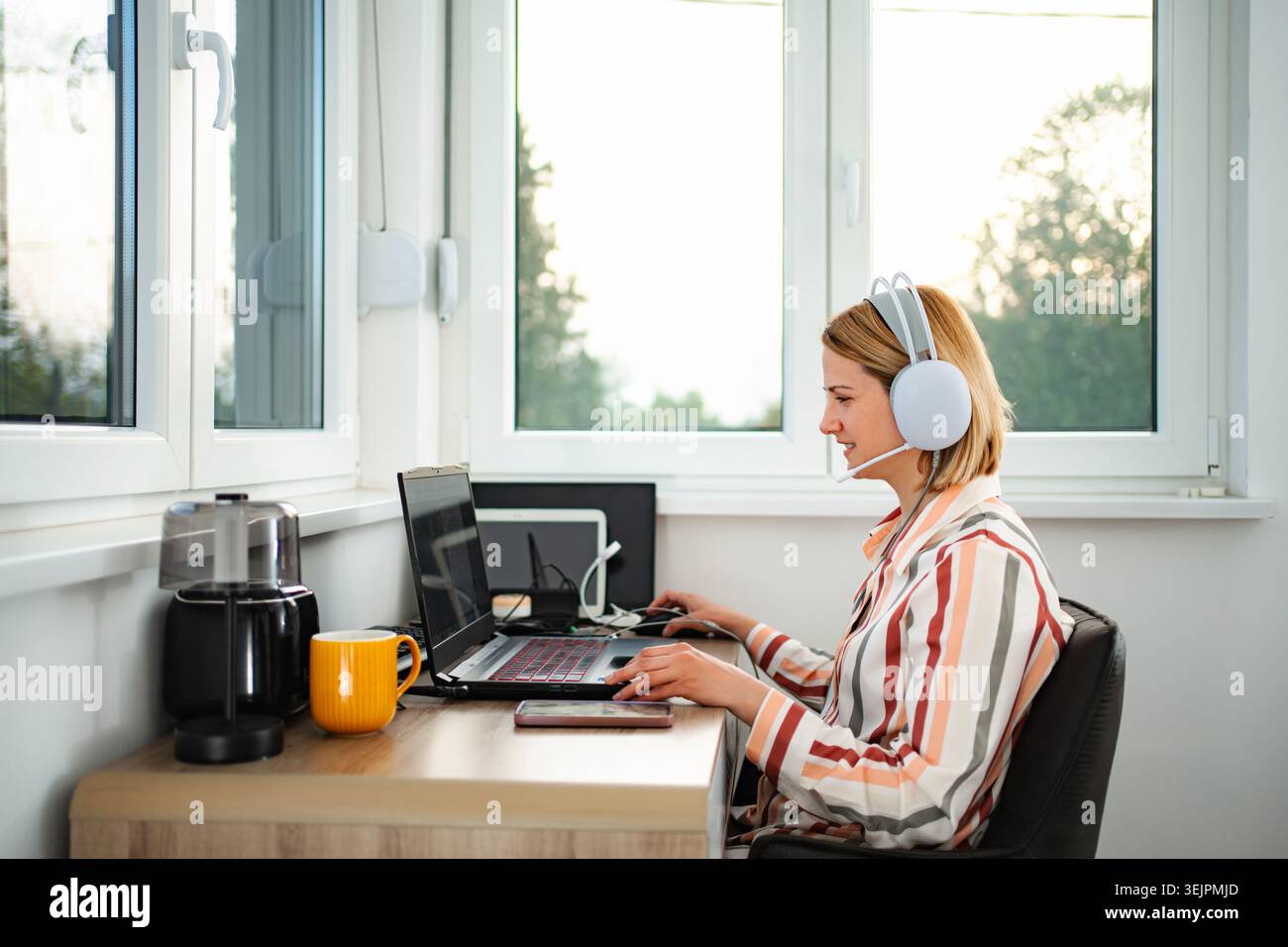 Woman working from home using laptop and headset Stock Photo