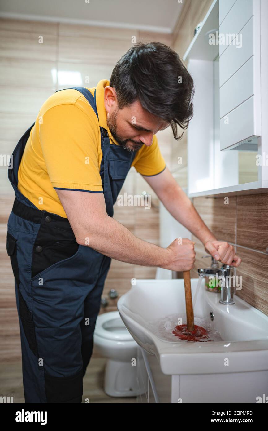 Plumber unclogging sink drain using plunger in bathroom Stock Photo