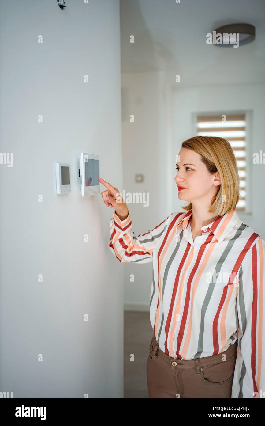 Woman adjusting smart home automation system on wall control panel Stock Photo