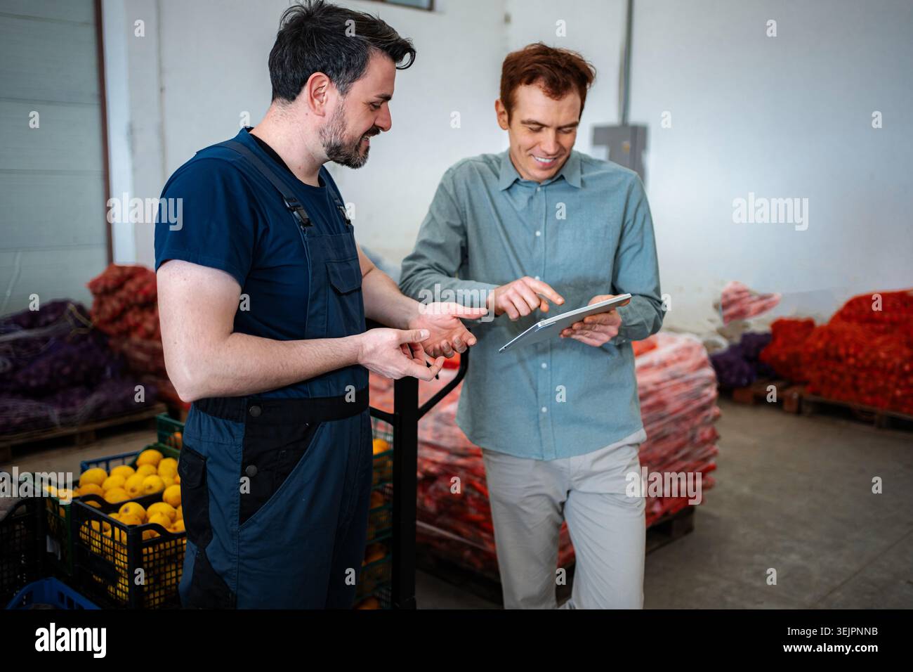 Two men working in a warehouse, using a digital tablet for inventory management Stock Photo
